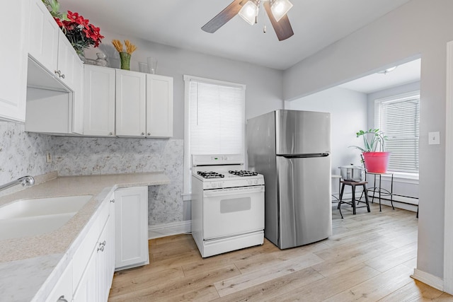 kitchen with a sink, white cabinetry, light wood-type flooring, freestanding refrigerator, and white gas range