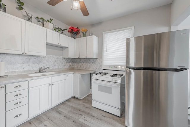 kitchen featuring freestanding refrigerator, gas range gas stove, light countertops, white cabinetry, and a sink