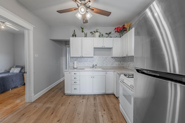 kitchen with white gas stove, light wood finished floors, light countertops, freestanding refrigerator, and a sink