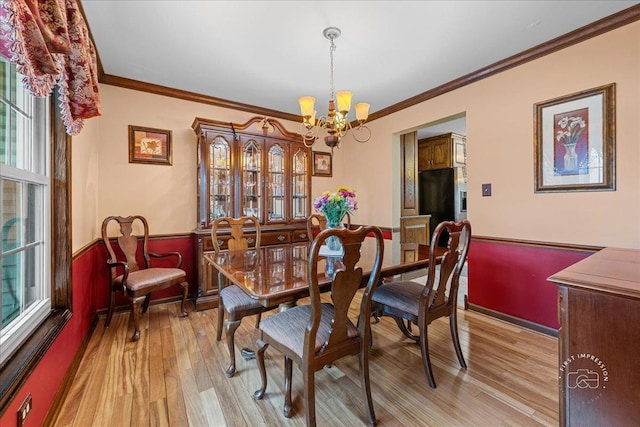 dining space with ornamental molding, light wood-type flooring, and a notable chandelier