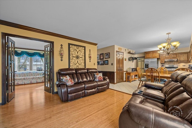 living room with light wood finished floors, wooden walls, a wainscoted wall, crown molding, and a notable chandelier