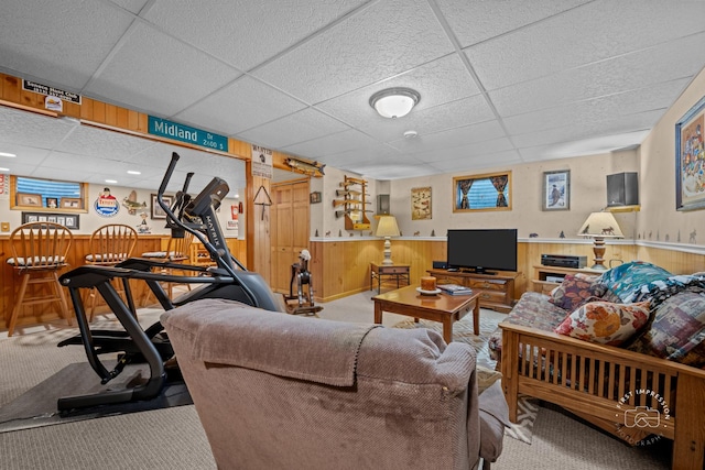 carpeted living room with a wainscoted wall, a dry bar, wood walls, and a drop ceiling