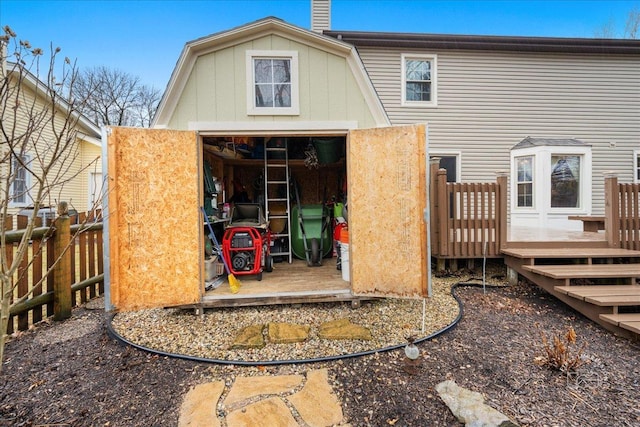 back of property featuring a gambrel roof, a storage unit, a deck, fence, and an outdoor structure