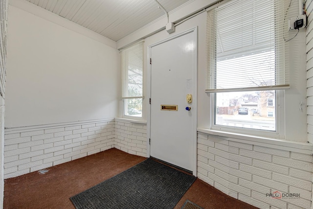 interior space with brick wall, wainscoting, and dark colored carpet