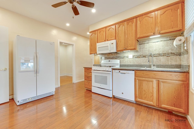 kitchen with white appliances, light wood finished floors, decorative backsplash, dark countertops, and a sink