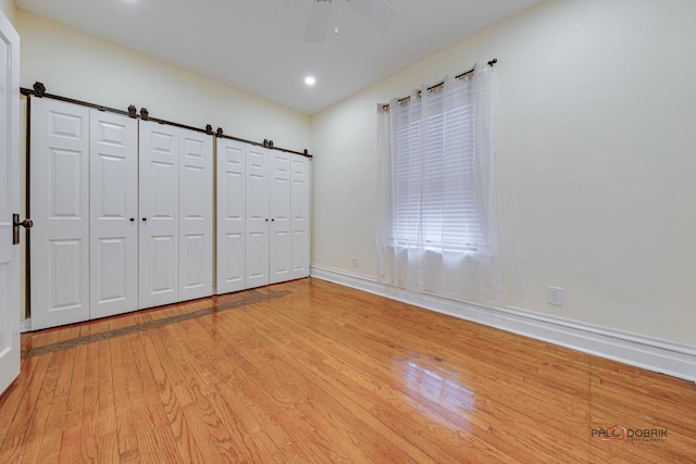 unfurnished bedroom with baseboards, ceiling fan, a barn door, and light wood-style floors