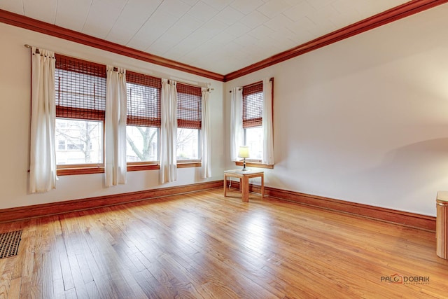 unfurnished room featuring light wood-type flooring, visible vents, crown molding, and baseboards