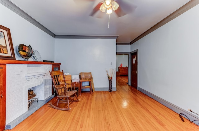 living area with ornamental molding, a brick fireplace, baseboards, and wood finished floors