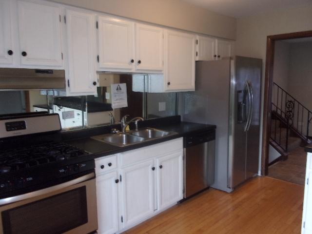 kitchen with white cabinets, dark countertops, appliances with stainless steel finishes, under cabinet range hood, and a sink