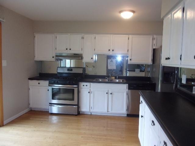 kitchen with stainless steel appliances, dark countertops, a sink, and under cabinet range hood