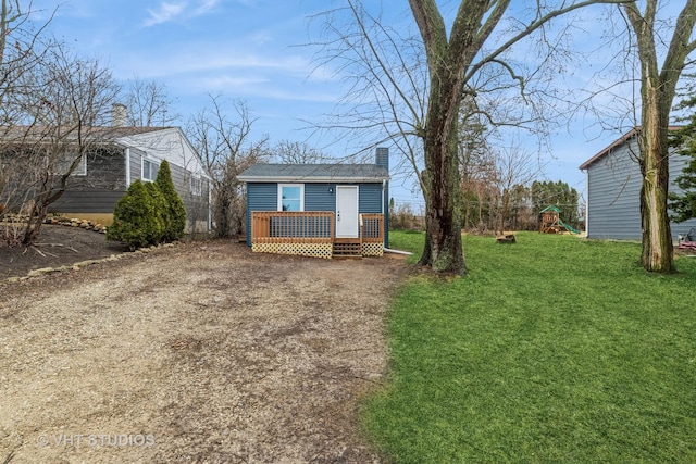 view of front facade featuring an outbuilding, a playground, driveway, a front lawn, and a chimney