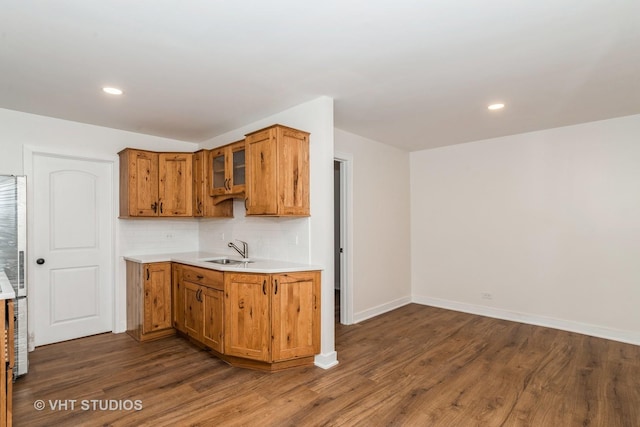 kitchen featuring dark wood finished floors, decorative backsplash, brown cabinets, light countertops, and a sink