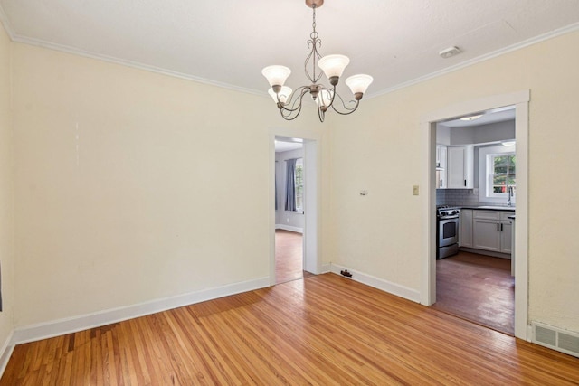 unfurnished dining area featuring crown molding, light wood-type flooring, a chandelier, and baseboards