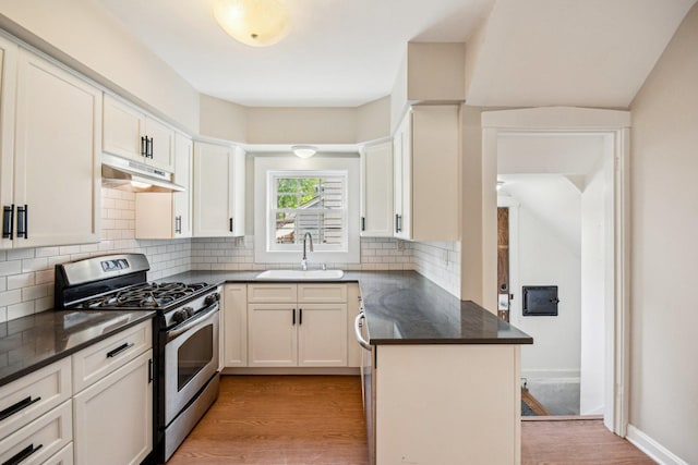 kitchen featuring gas stove, a sink, under cabinet range hood, light wood-type flooring, and dark countertops