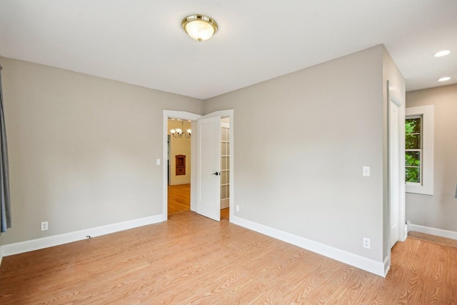 spare room featuring a chandelier, light wood finished floors, baseboards, and recessed lighting
