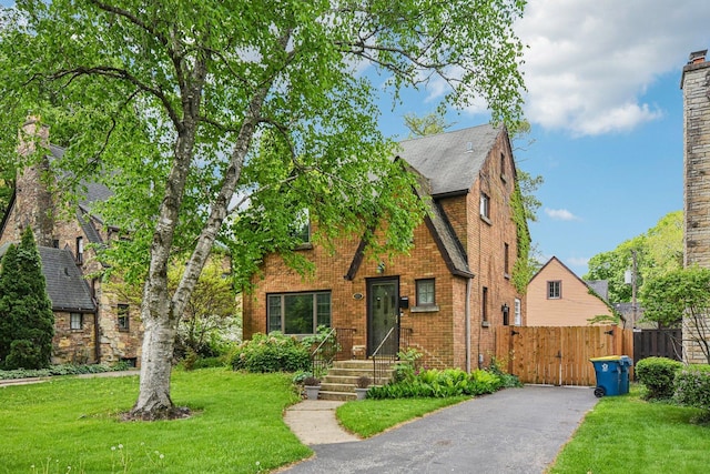 english style home featuring brick siding, driveway, and roof with shingles