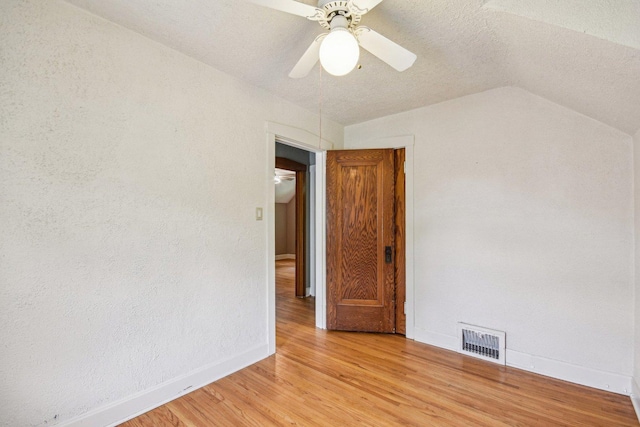 spare room with light wood finished floors, baseboards, lofted ceiling, ceiling fan, and a textured ceiling