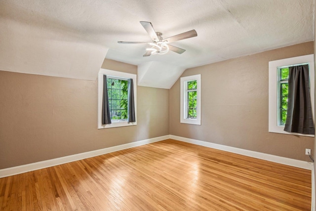 additional living space with light wood finished floors, baseboards, lofted ceiling, ceiling fan, and a textured ceiling