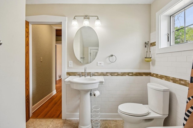 bathroom featuring tile walls, toilet, tile patterned floors, and a wainscoted wall