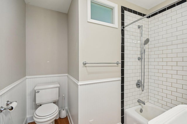 bathroom with a wainscoted wall, toilet, and shower / washtub combination