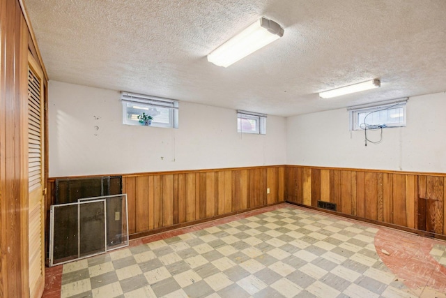 basement with light floors, a textured ceiling, wood walls, and wainscoting