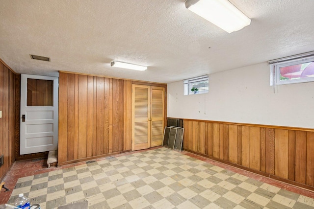 basement featuring a textured ceiling, wooden walls, and light flooring
