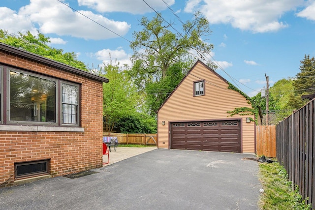 view of property exterior with an outdoor structure, a detached garage, brick siding, and fence