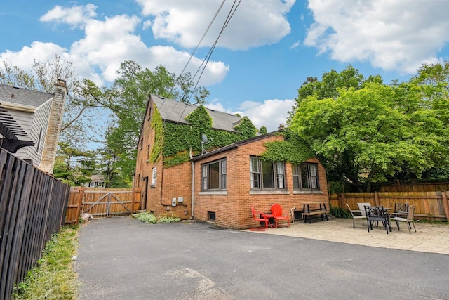 view of side of property with brick siding, a patio area, a fenced backyard, and a gate