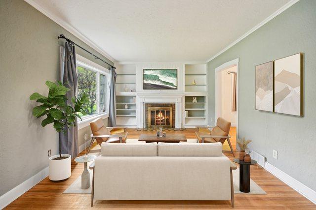 living room featuring ornamental molding, wood finished floors, a lit fireplace, baseboards, and built in features
