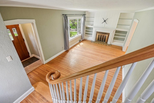 staircase with crown molding, wood finished floors, a glass covered fireplace, baseboards, and built in shelves