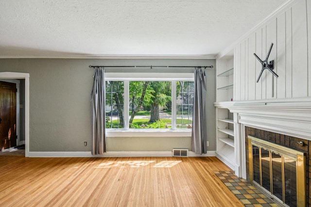 unfurnished living room featuring wood finished floors, baseboards, a fireplace, crown molding, and a textured ceiling
