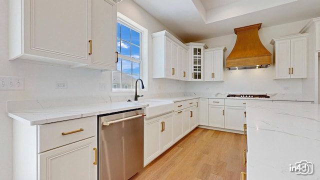 kitchen featuring premium range hood, a sink, white cabinets, light wood-type flooring, and dishwasher