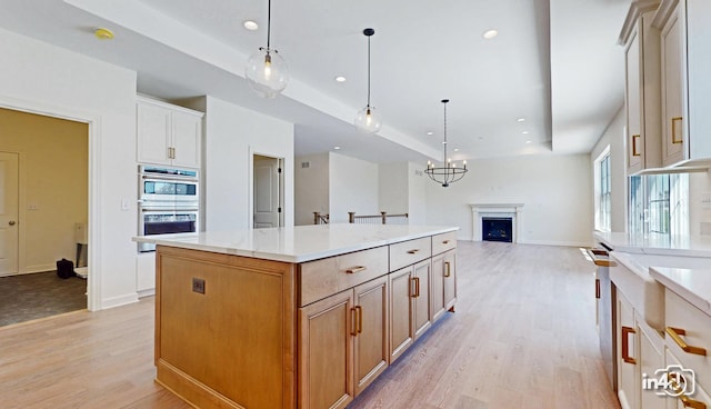 kitchen featuring double oven, a center island, a raised ceiling, and light wood-style floors