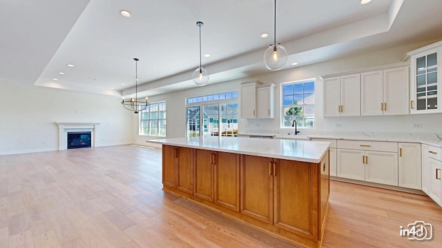 kitchen with light wood finished floors, a raised ceiling, a sink, and a center island