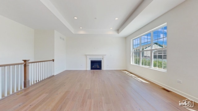 unfurnished living room with a tray ceiling, recessed lighting, visible vents, wood finished floors, and baseboards