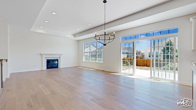 unfurnished living room featuring recessed lighting, baseboards, light wood-type flooring, a tray ceiling, and a glass covered fireplace