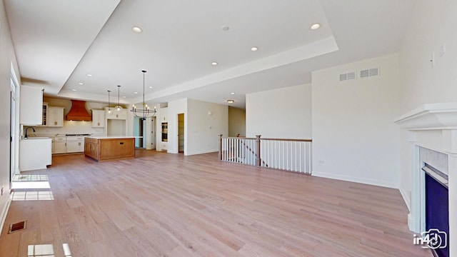 unfurnished living room featuring a fireplace, a raised ceiling, visible vents, light wood-type flooring, and baseboards