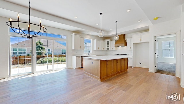 kitchen with light wood-style flooring, a kitchen island, custom exhaust hood, light countertops, and a sink