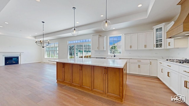 kitchen with a kitchen island, open floor plan, custom exhaust hood, light wood-type flooring, and a sink