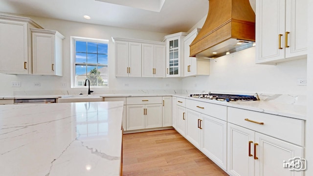 kitchen featuring light wood finished floors, white cabinets, stainless steel appliances, premium range hood, and a sink