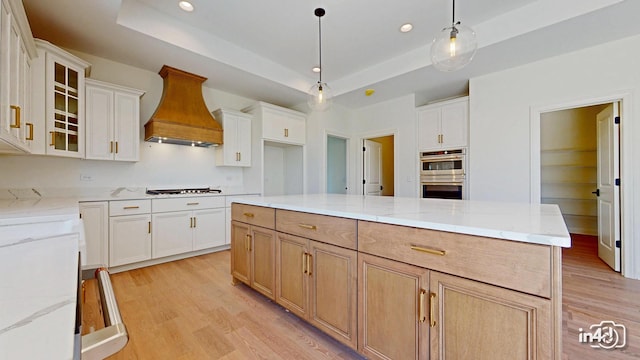 kitchen with a raised ceiling, light wood-type flooring, double oven, and custom exhaust hood