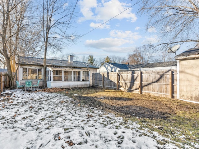 snow covered back of property with a sunroom, fence, and a chimney