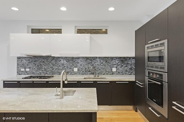 kitchen with modern cabinets, appliances with stainless steel finishes, light stone counters, and a sink