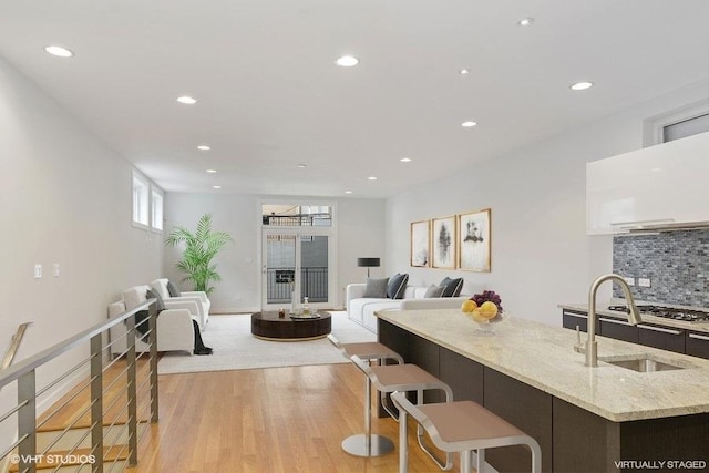 kitchen with light wood finished floors, tasteful backsplash, light stone countertops, a sink, and recessed lighting