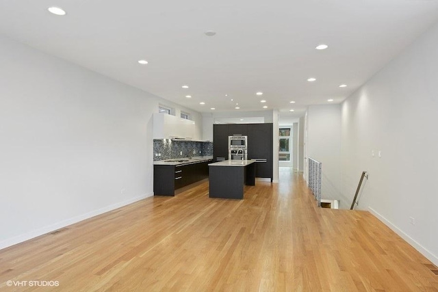 kitchen with dark cabinets, light countertops, light wood-type flooring, tasteful backsplash, and modern cabinets