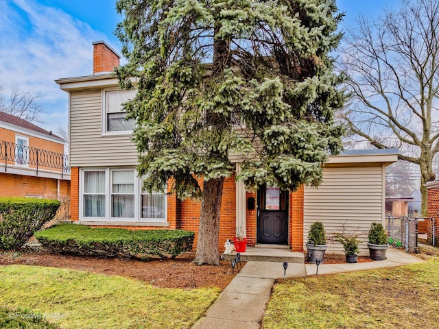 view of front of house with brick siding, fence, a chimney, and a front lawn