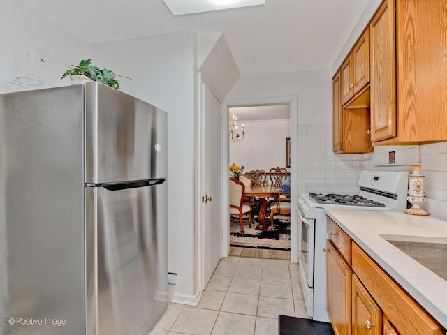 kitchen with light tile patterned flooring, backsplash, freestanding refrigerator, brown cabinets, and gas range gas stove