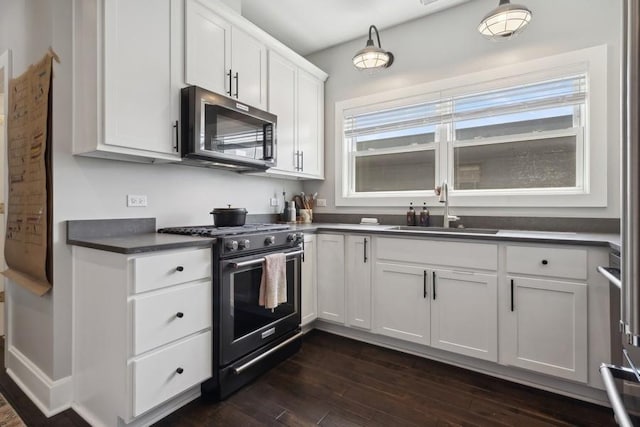 kitchen featuring dark countertops, dark wood-style floors, stainless steel microwave, gas range oven, and a sink