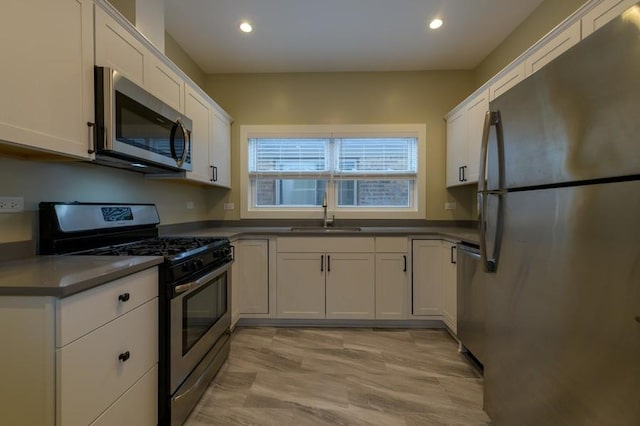 kitchen featuring recessed lighting, stainless steel appliances, a sink, white cabinets, and dark countertops