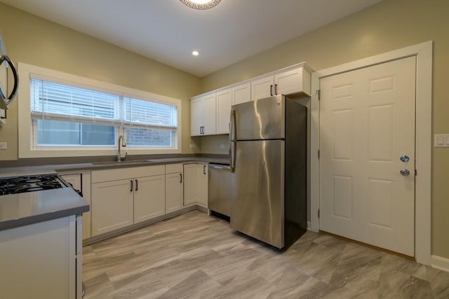 kitchen with stainless steel appliances, dark countertops, a sink, and white cabinets